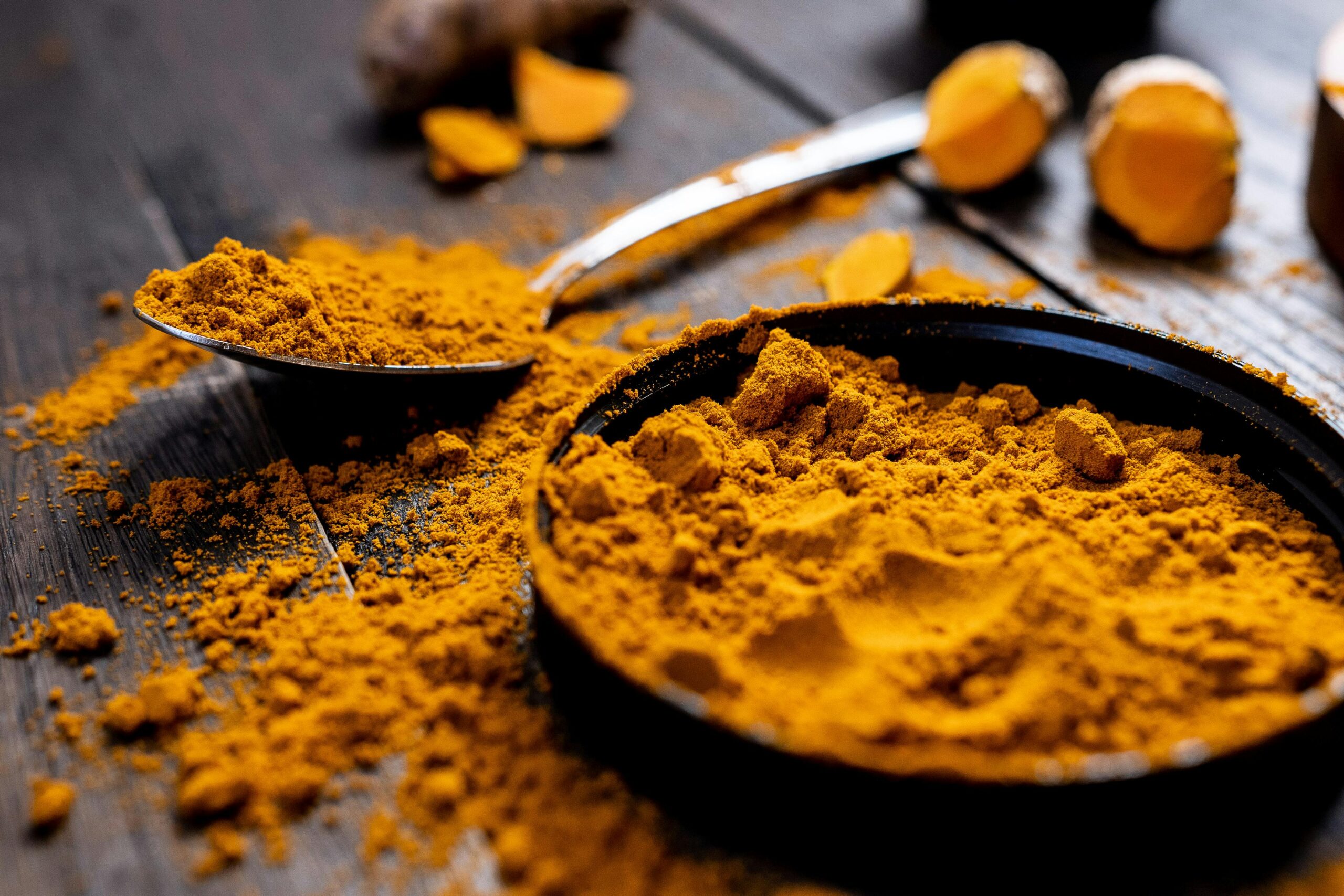 Close-up of vibrant turmeric powder with root on rustic wooden table, emphasizing texture and color.