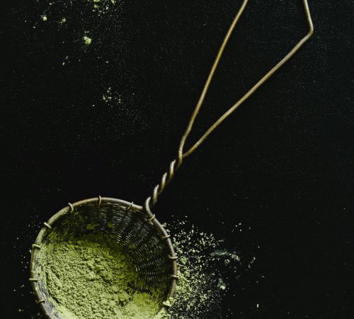 Vintage sieve filled with green matcha powder, captured from above on dark background.